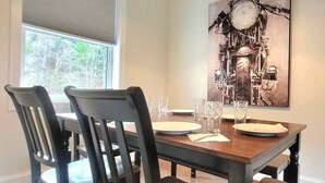 A dining table with four chairs, a painting on the wall, and a window with blinds. - The Traveler on Main - Suite #6- Across the Street from Back of the Dragon! (Tazewell)