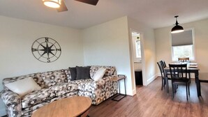 A living room with a patterned sofa, a wooden coffee table, a dining area with a table and chairs, and a compass wall decoration. - The Traveler on Main - Suite #6- Across the Street from Back of the Dragon! (Tazewell)