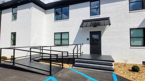 A modern two-story building with a white exterior, black-framed windows, and a black awning over the entrance.