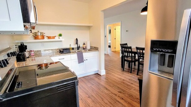 A modern kitchen with a stove, oven, and refrigerator. There is a dining area with chairs and a table.