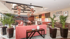 Un moderno vestíbulo de hotel con una zona de estar central, ventanas amplias y plantas decorativas.