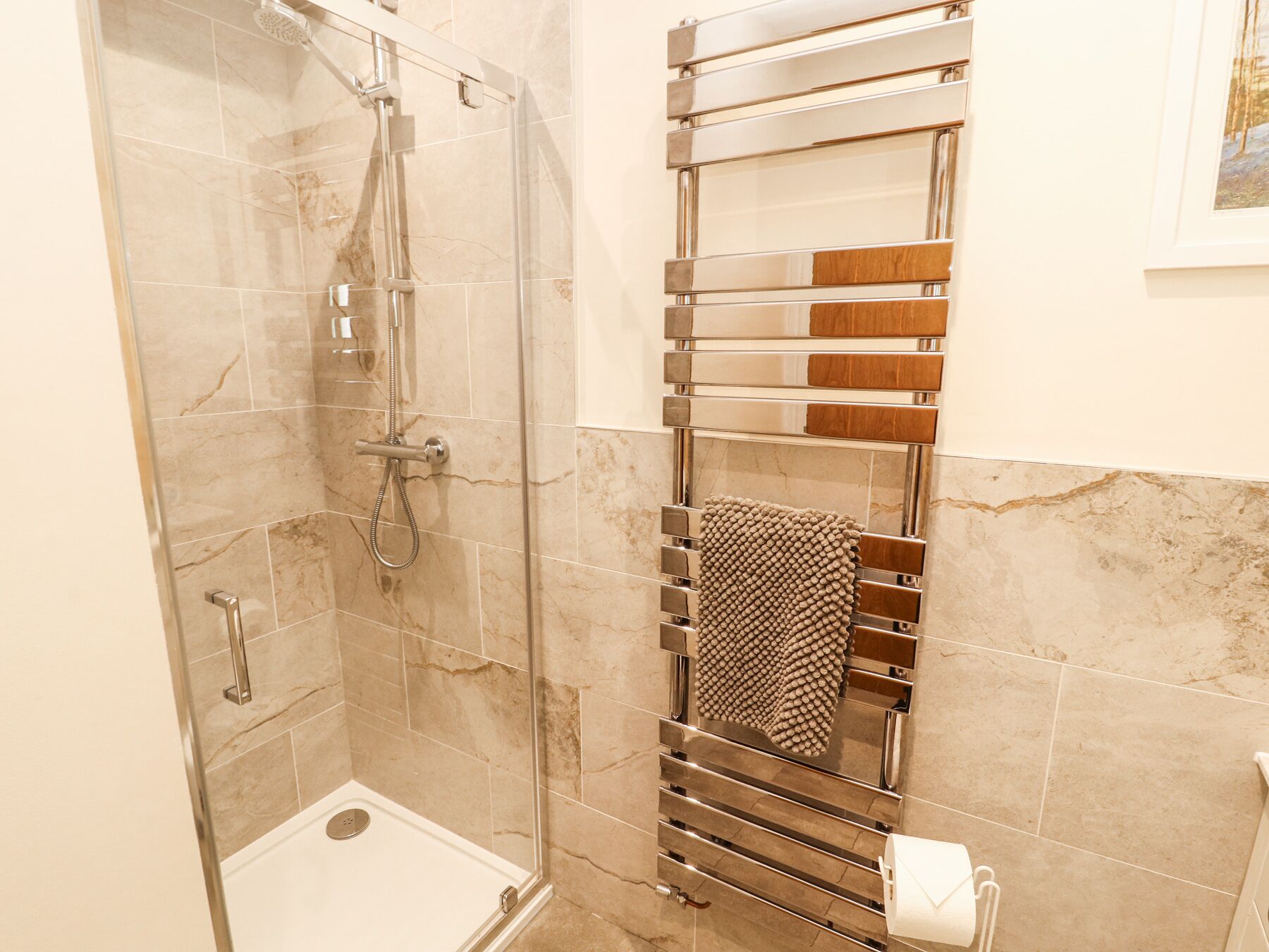 Ein modernes Badezimmer mit Duschkabine aus Glas, einem chromfarbenen Handtuchhalter und einer Wand mit Marmorfliesen.