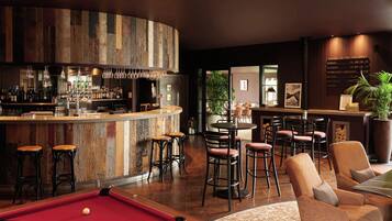 A bar area with a pool table, bar stools, and a seating area with chairs.