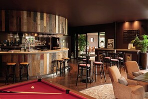 Zona de bar con mesa de billar, taburetes y un espacio de estar con sillas.
