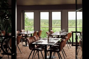 Un comedor con mesas y sillas, ventanas amplias y vistas a zonas verdes.