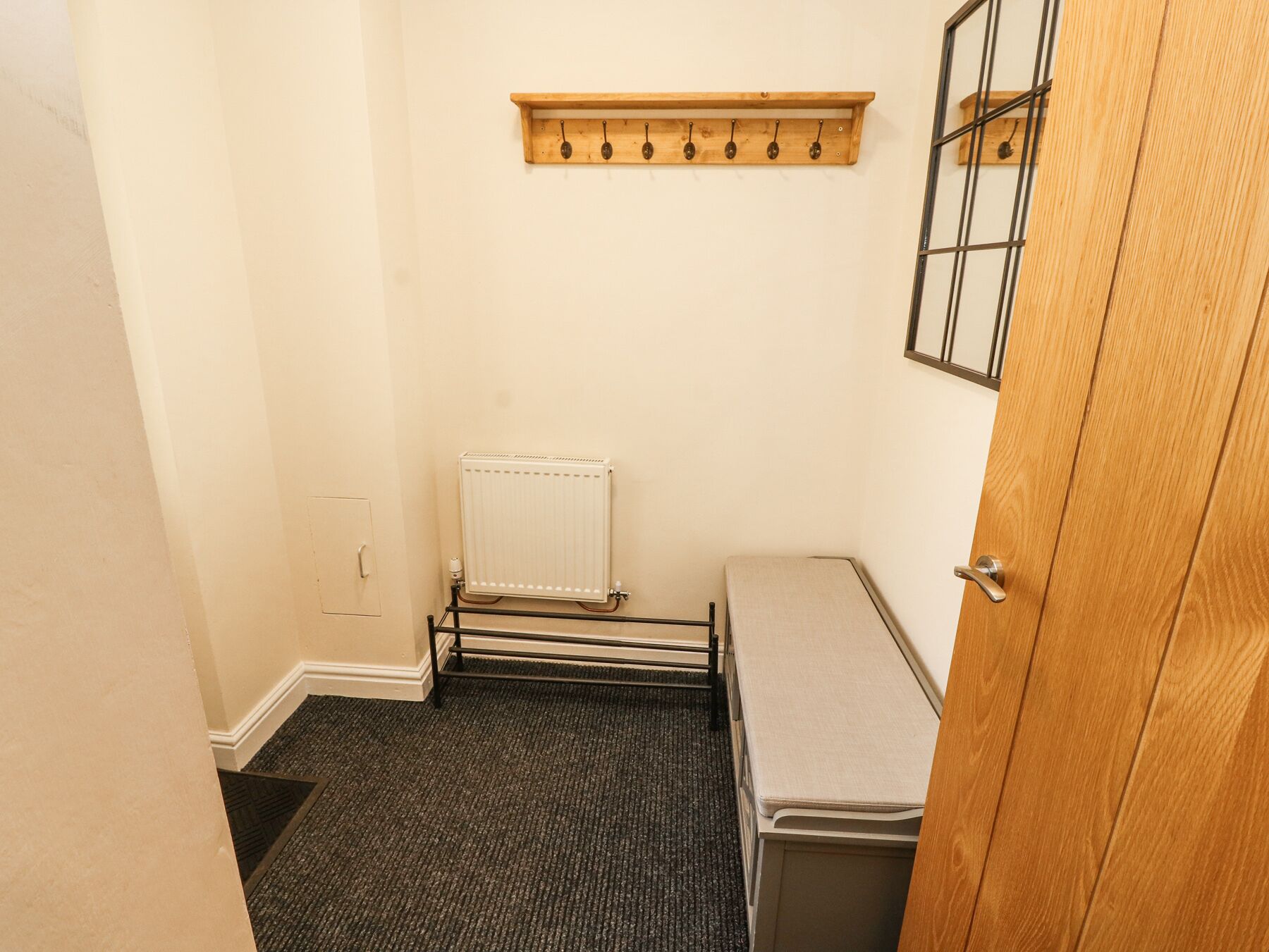 A small, narrow room with a radiator, a wooden shelf with hooks, and a door.