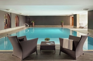 Piscina com duas cadeiras de vime e uma pequena mesa, cercada por paredes escuras e piso de azulejos.