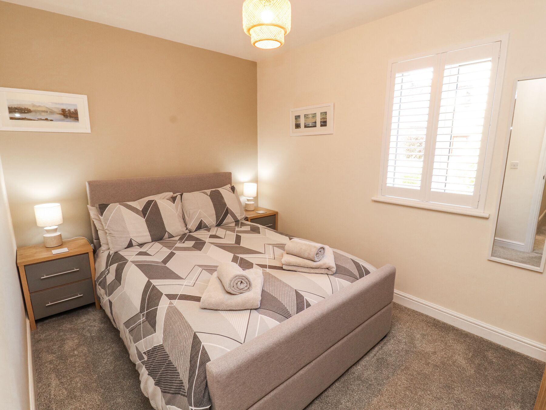 A bedroom with a bed, nightstands, a lamp, a window with blinds, and a wall-mounted picture.