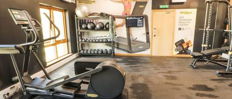A gym with treadmills, a wall-mounted elliptical, free weights, and a poster of a woman exercising.