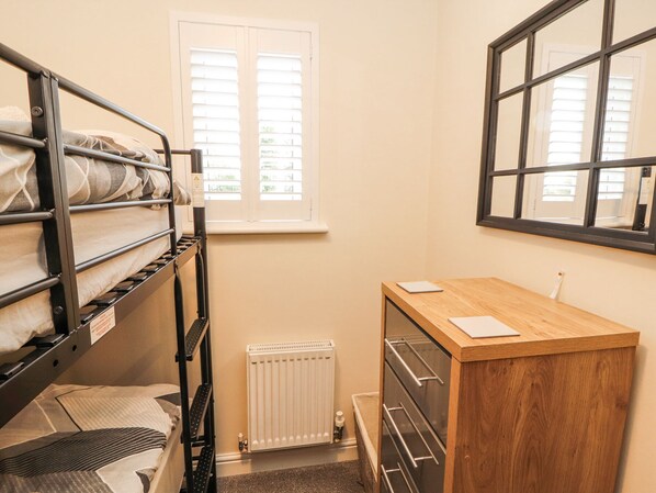 A compact room with bunk beds, a wooden desk, a radiator, and a window with blinds. - Squirrel Cottage (Penrith)
