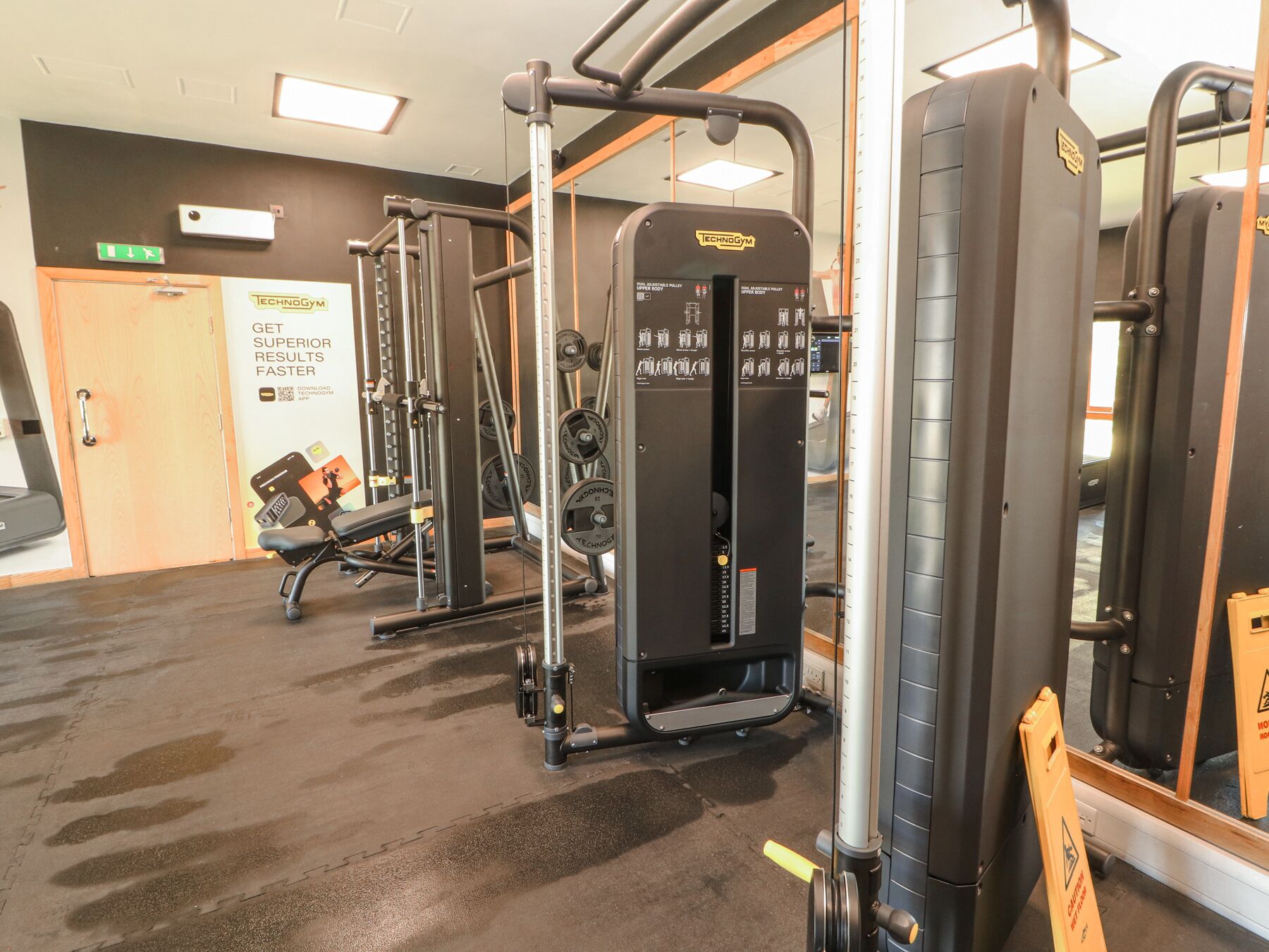 Une salle de sport équipée de divers appareils d’exercice, d’un banc et d’un miroir.