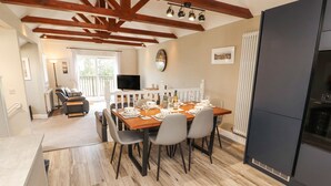 Un comedor con una mesa de madera dispuesta para cuatro personas, rodeada de sillas. Un televisor está montado en la pared sobre la mesa.