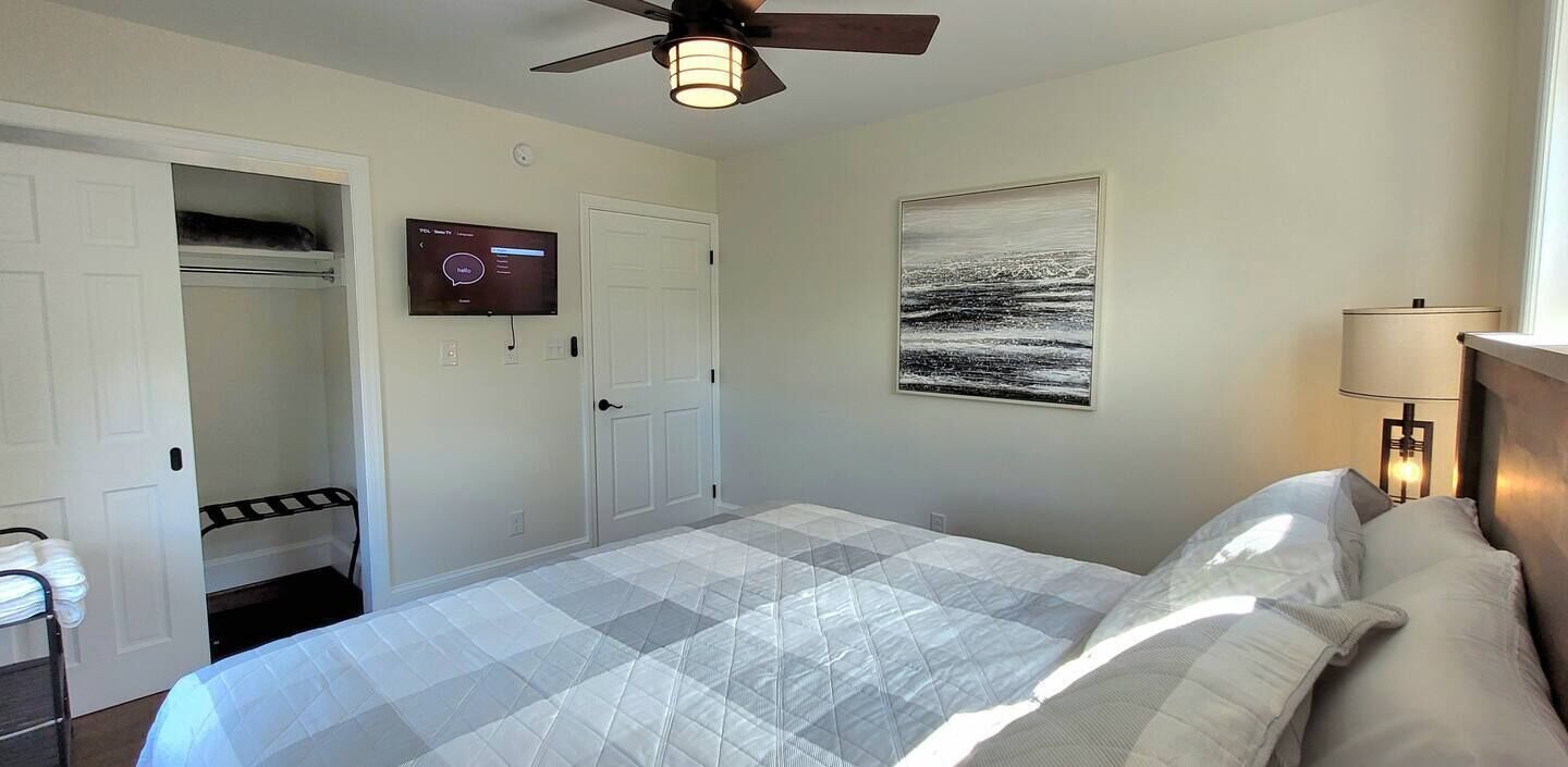A bedroom with a bed, a ceiling fan, a TV on the wall, and a painting.