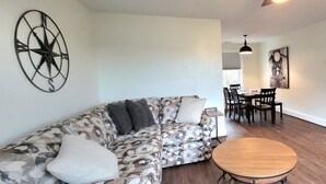 Un salon avec un canapé à motifs, une table ronde en bois et un coin repas comprenant des chaises et une table.