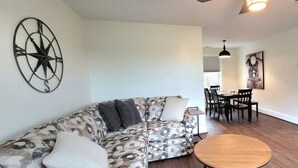 A living room with a patterned sofa, a round wooden table, and a dining area with chairs and a table. - The Traveler On Main - Suite #5- Across the Street from Back of the Dragon! (Tazewell)