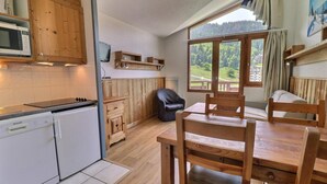 A compact kitchen with a microwave, a small refrigerator, wooden cabinets, and a dining area with a table and chairs. - 50m from ski slopes, 7th floor, balcony, ski locker, 25m², La Tania (Courchevel)