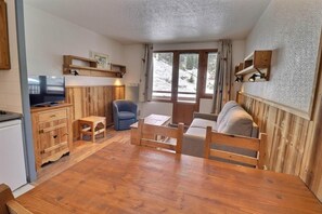 A cozy room with a wooden table, a sofa, a TV, and a chair. - 150m from resort center, 3rd floor, balcony, ski locker, 25m², La Tania (Courchevel)