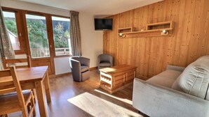 Una sala de estar con muebles de madera, un sofá, un televisor en la pared y un comedor con una mesa y sillas.
