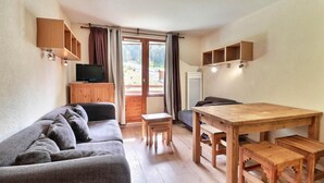 A cozy living room with a sofa, a wooden dining table, and a TV on a wooden cabinet.