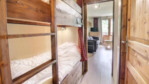 A bunk bed room with wooden walls and a door leading to a living area with a sofa and a TV.