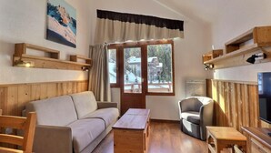 A cozy room with a wooden sofa, a small table, a chair, a TV, and a window with curtains. - 50m from ski slopes, 5th floor, balcony, ski locker, 31m², La Tania (Courchevel)