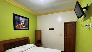 Une chambre à coucher avec un lit, une table de chevet, un téléviseur fixé au mur, une porte et un tableau accroché au mur.