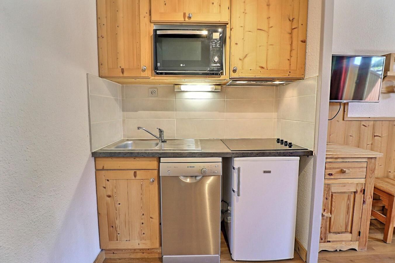A compact kitchen with wooden cabinets, a Bosch dishwasher, a white refrigerator, and a microwave.