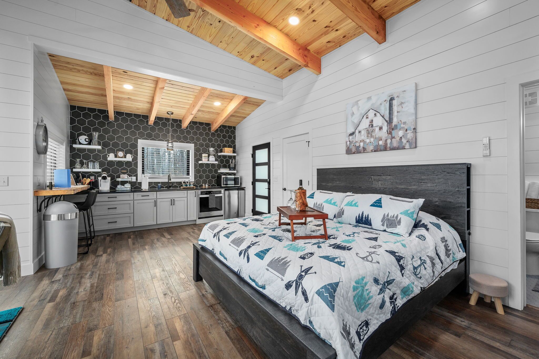 Ein Schlafzimmer mit einem großen Bett, Holzboden, einer Küchenzeile und einer weißen Wand mit sechseckigem Muster.
