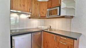 A compact kitchen with wooden cabinets, a stainless steel refrigerator, a microwave, and a sink. - 50m from ski slopes, 2nd floor, balcony, ski locker, 31m², La Tania (Courchevel)