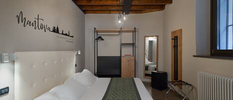 Una habitación de hotel con cama, mesita de noche, lámpara colgante, radiador y ventana.