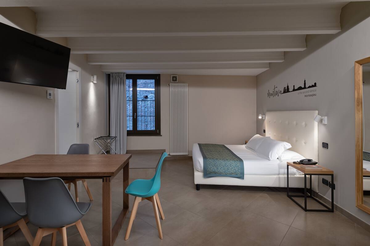 Habitación de hotel con cama, escritorio, dos sillas, televisor, ventana con vista y un mural del horizonte urbano en la pared.