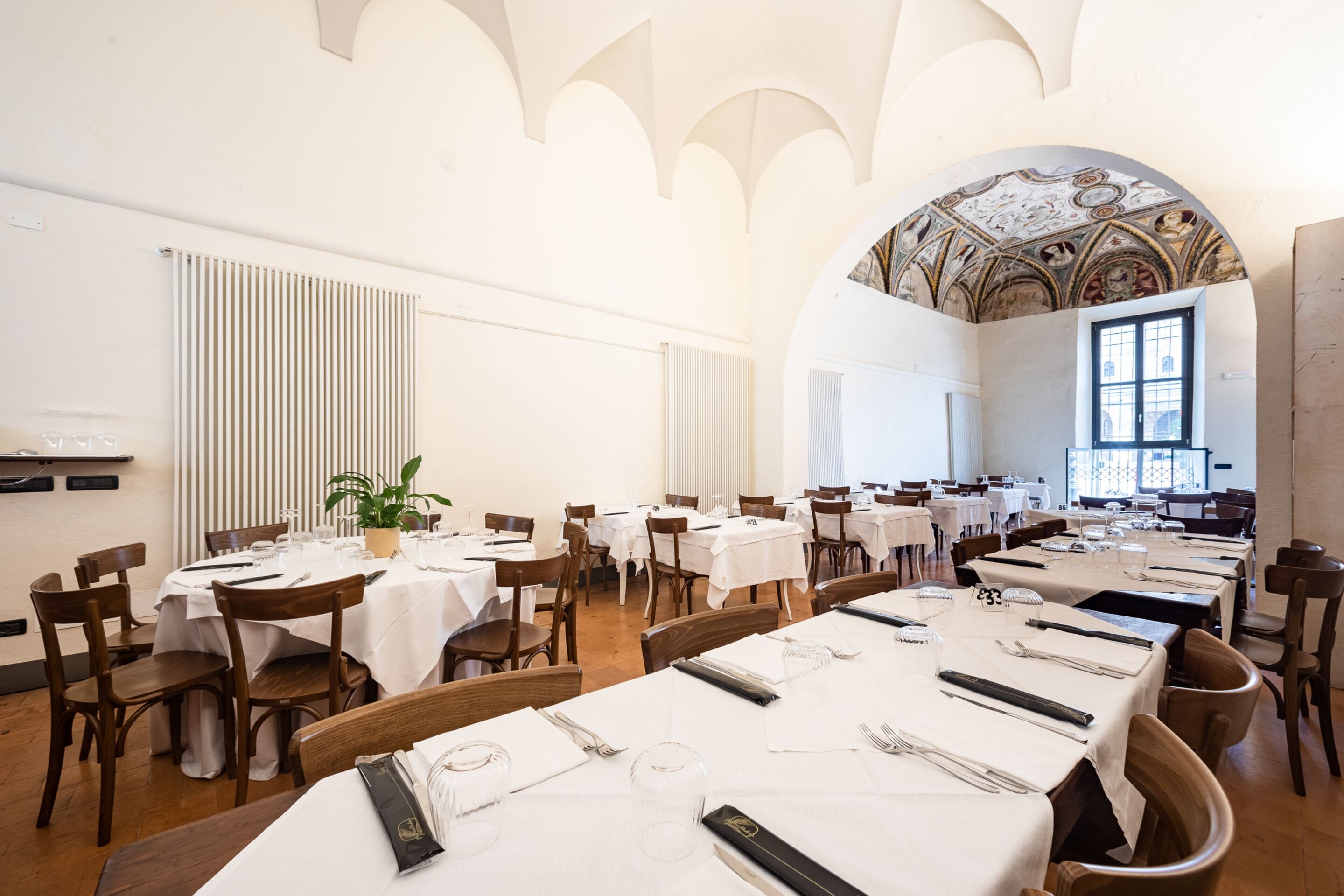 Un comedor amplio con varias mesas dispuestas para comer, con manteles blancos y sillas de madera.