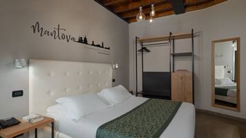 Une chambre bien rangée, avec un lit, une table de chevet, un miroir et un mur orné d’une fresque représentant un paysage urbain.