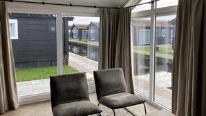 Una habitación con dos sillas grises, un ventanal con cortinas y vistas a casas y un canal.