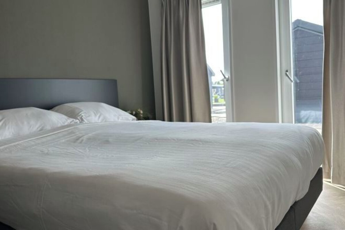 Una cama bien tendida en una habitación con un ventanal y cortinas.
