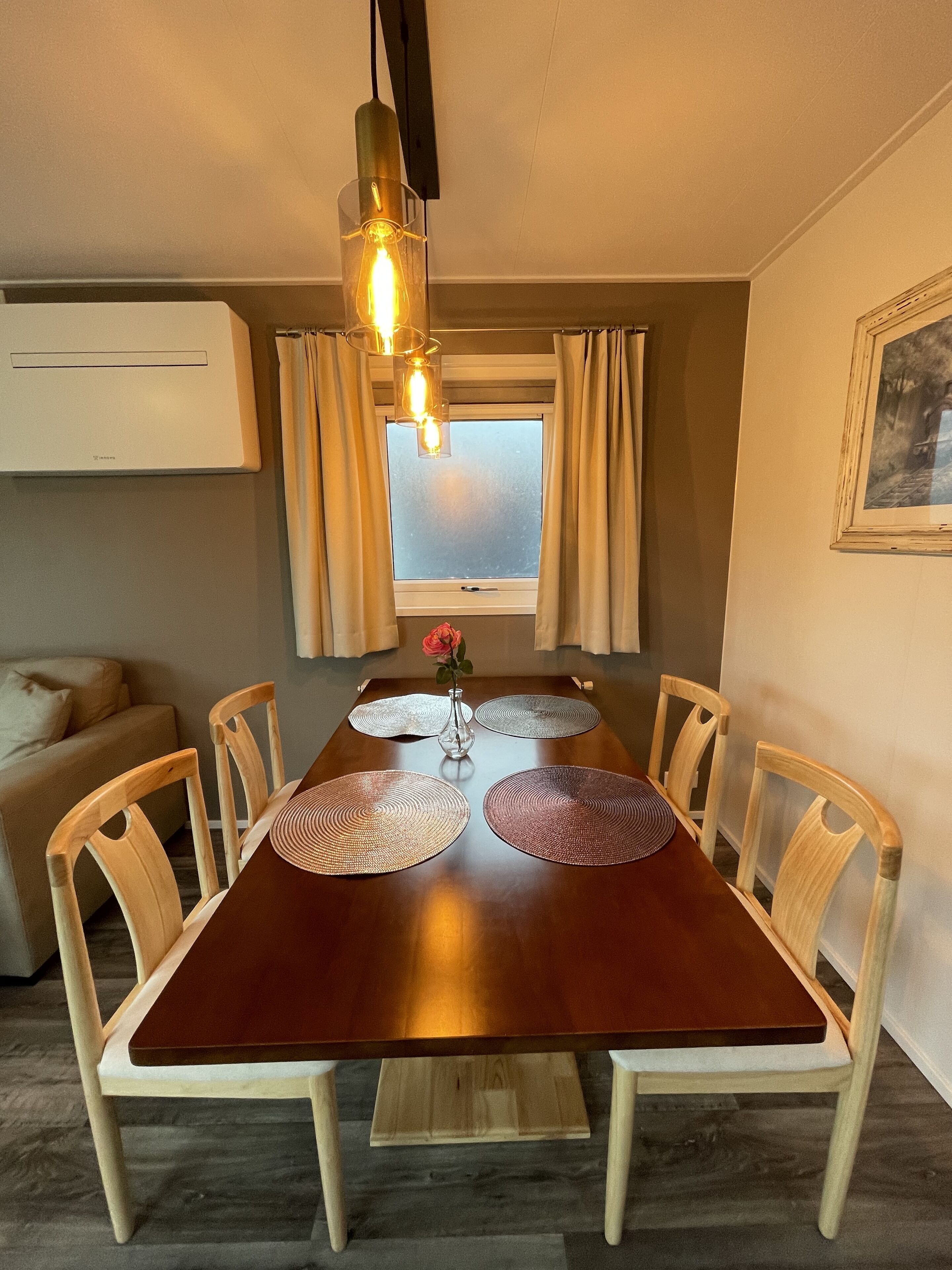 A dining area with a wooden table, four chairs, a vase with a flower, and a pendant light.