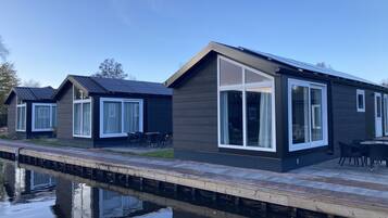 Een rij moderne, donkergekleurde huizen met grote ramen en een steiger die in het rustige water reikt.