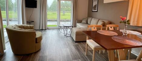 Una sala de estar moderna con un sofá, una mesa de comedor con sillas y un televisor montado en la pared.
