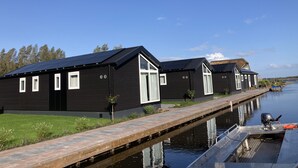 Una hilera de edificios negros con ventanas y puertas blancas, unidos por un pasarela de madera sobre el agua.