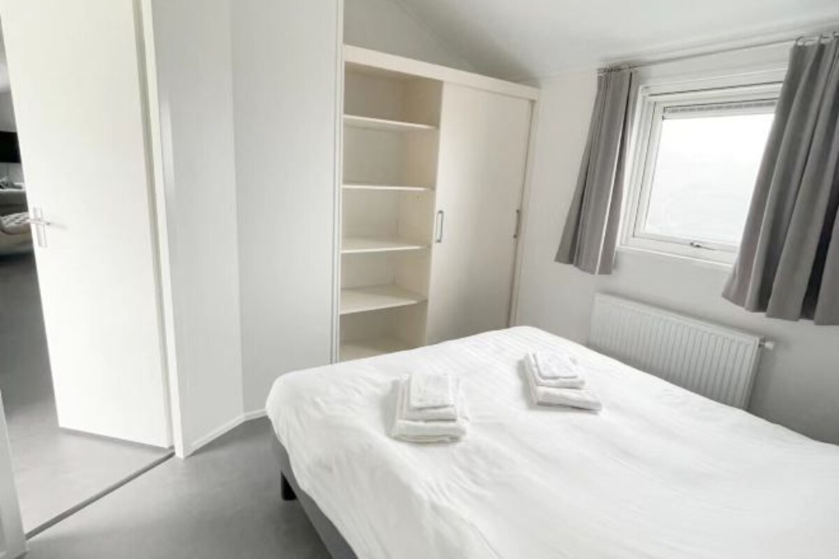 Un dormitorio con cama, armario y ventana con cortinas.