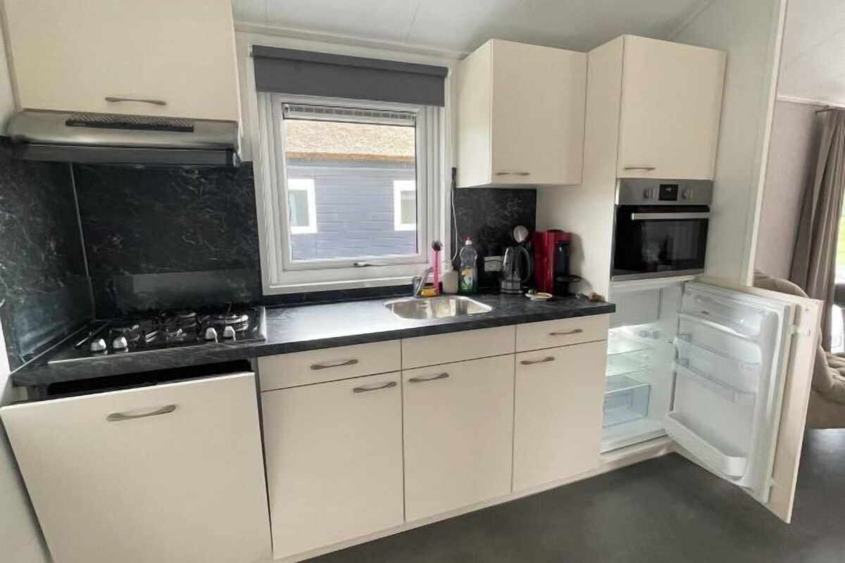 A compact kitchen with white cabinets, a black countertop, a gas stove, a built-in oven, and a refrigerator.