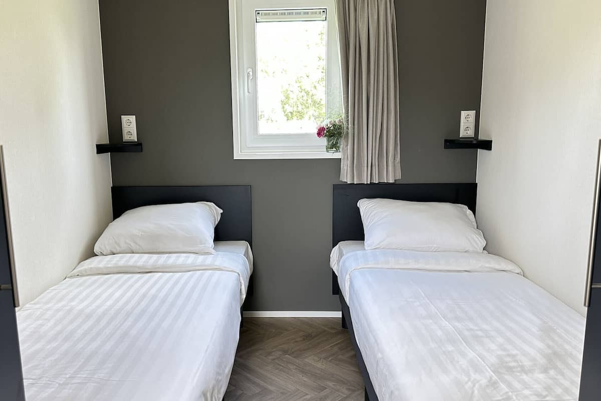 Una habitación con dos camas individuales, una ventana con vistas y un pequeño estante con toma de corriente.