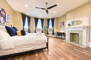 Camera da letto con un letto, una ventola a soffitto, un camino e ampie finestre con tende.