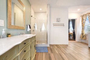 A modern bathroom with a large mirror, two sinks, a shower, and a wooden floor.