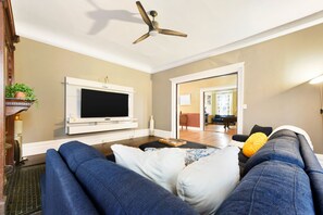 Un soggiorno con televisione a schermo piatto, ventilatore a soffitto e divano con cuscini.