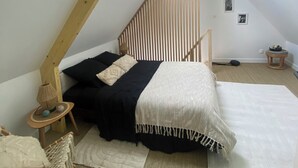 A loft bedroom with a sloped ceiling, a skylight, a bed with black and white bedding, a macramé chair, and a small wooden side table. - Maison 2 à 6 Pers - En Plein Coeur de la Capitale du lin ! (Yvecrique)