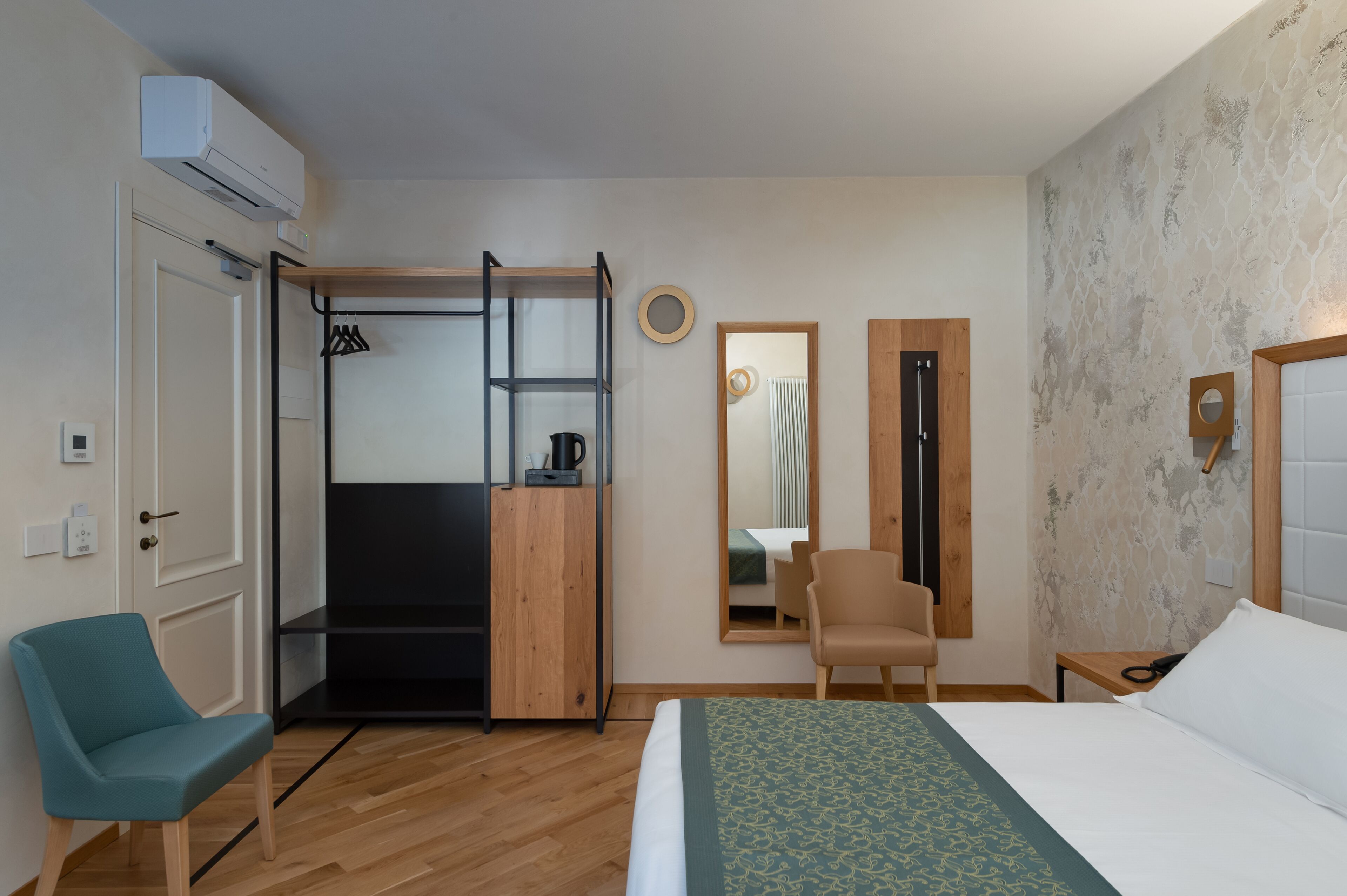 Een hotelkamer met een bed, een stoel, een kledingkast, een spiegel en een klein tafeltje.