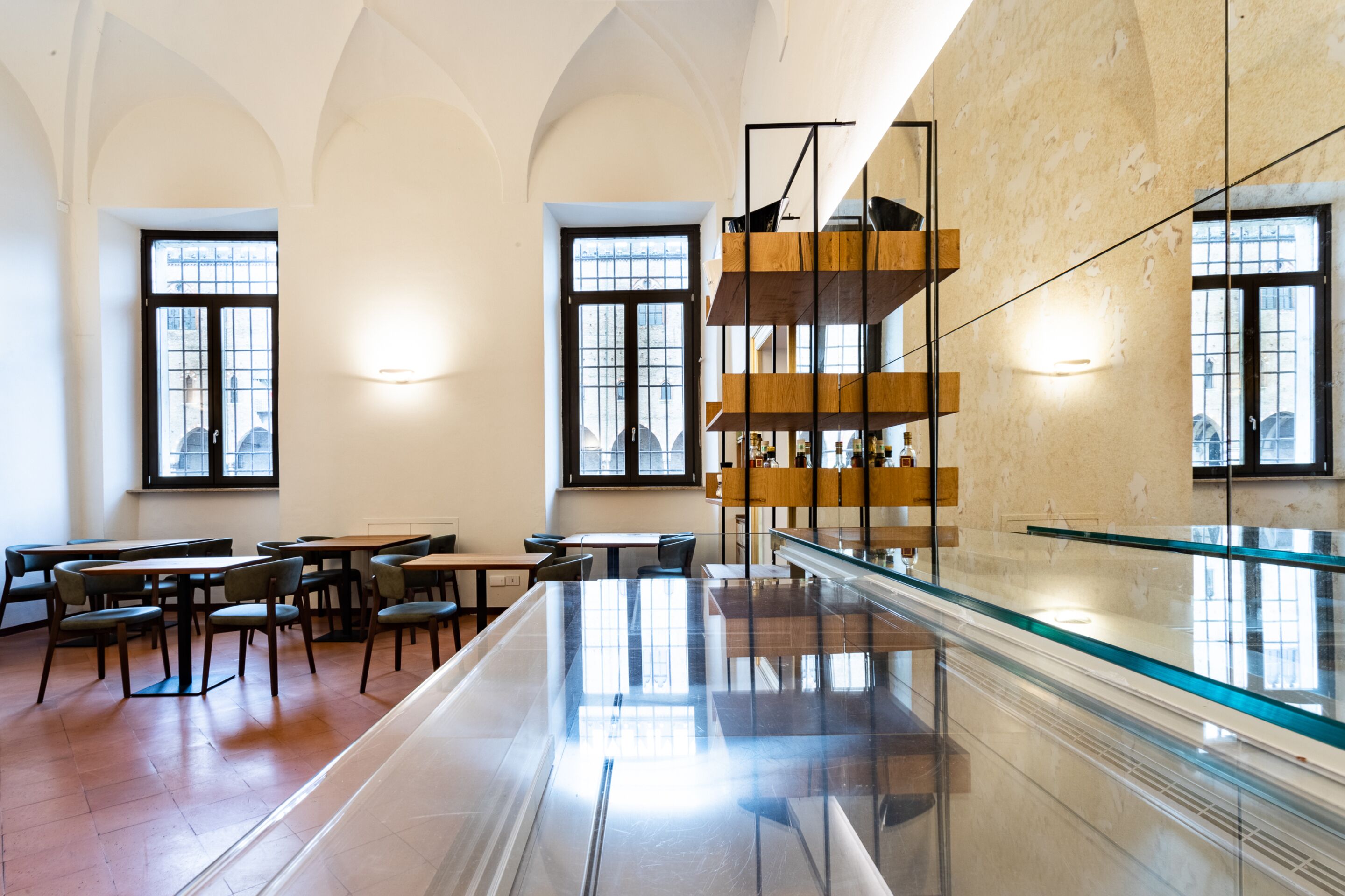 Una biblioteca espaciosa con techos altos, ventanas grandes y una mesa de vidrio en el centro.