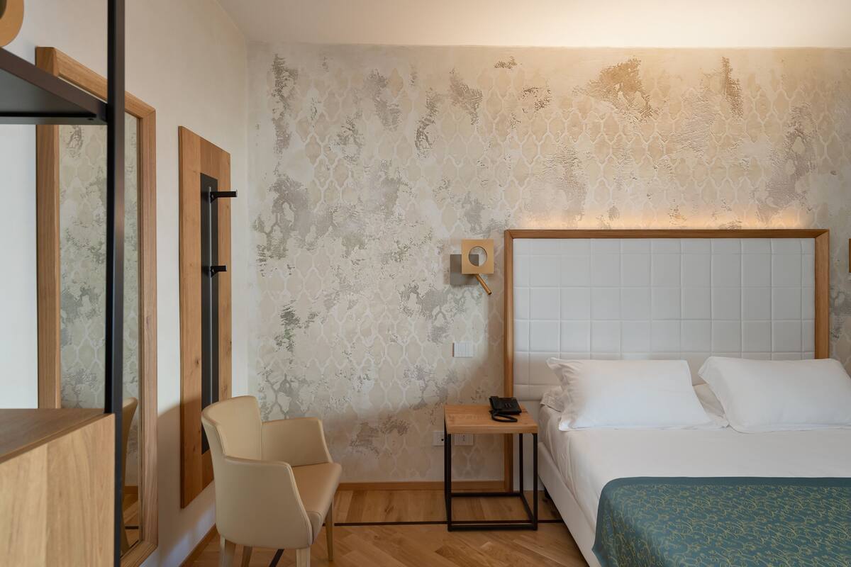 Ein Hotelzimmer mit einem Bett, einem Sessel, einem kleinen Tisch mit Telefon und einer Wand mit Strukturmuster.