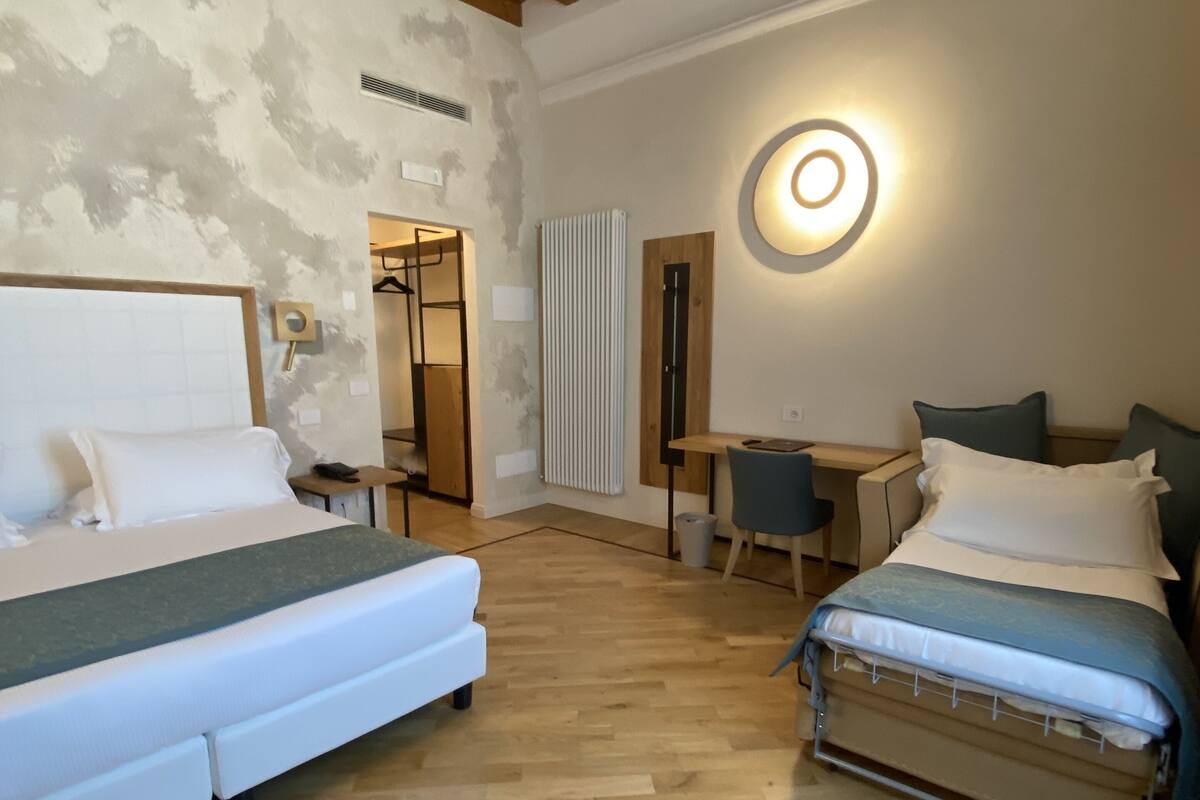 Ein Zimmer mit zwei Betten, einem Schreibtisch und einem Stuhl. Es gibt einen Heizkörper und eine runde Leuchte an der Wand.